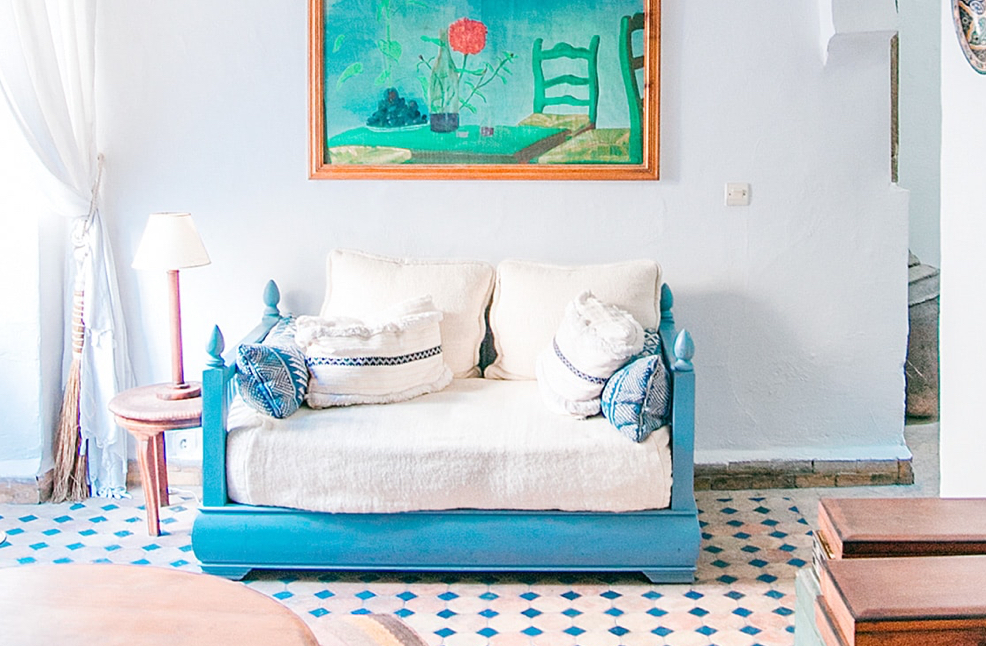 A blue and white couch in a brightly daylit room with a colourful painting hanging above