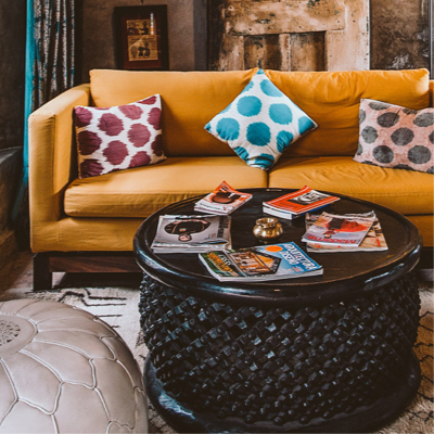 A tan leather couch with three polkadot pillow on it and a round black coffee table infront of the couch.