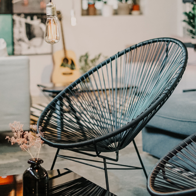 A black alcapulco chair sitting in a living room underneath a hanging lightbulb lamp.